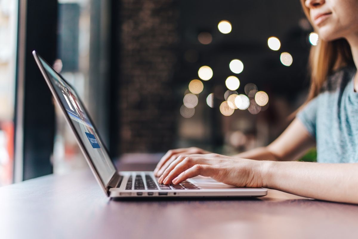 Close up crooped shot of young casually dressed female freelancer sitting at loft food court working on her laptop. Girl making online order in internet store.